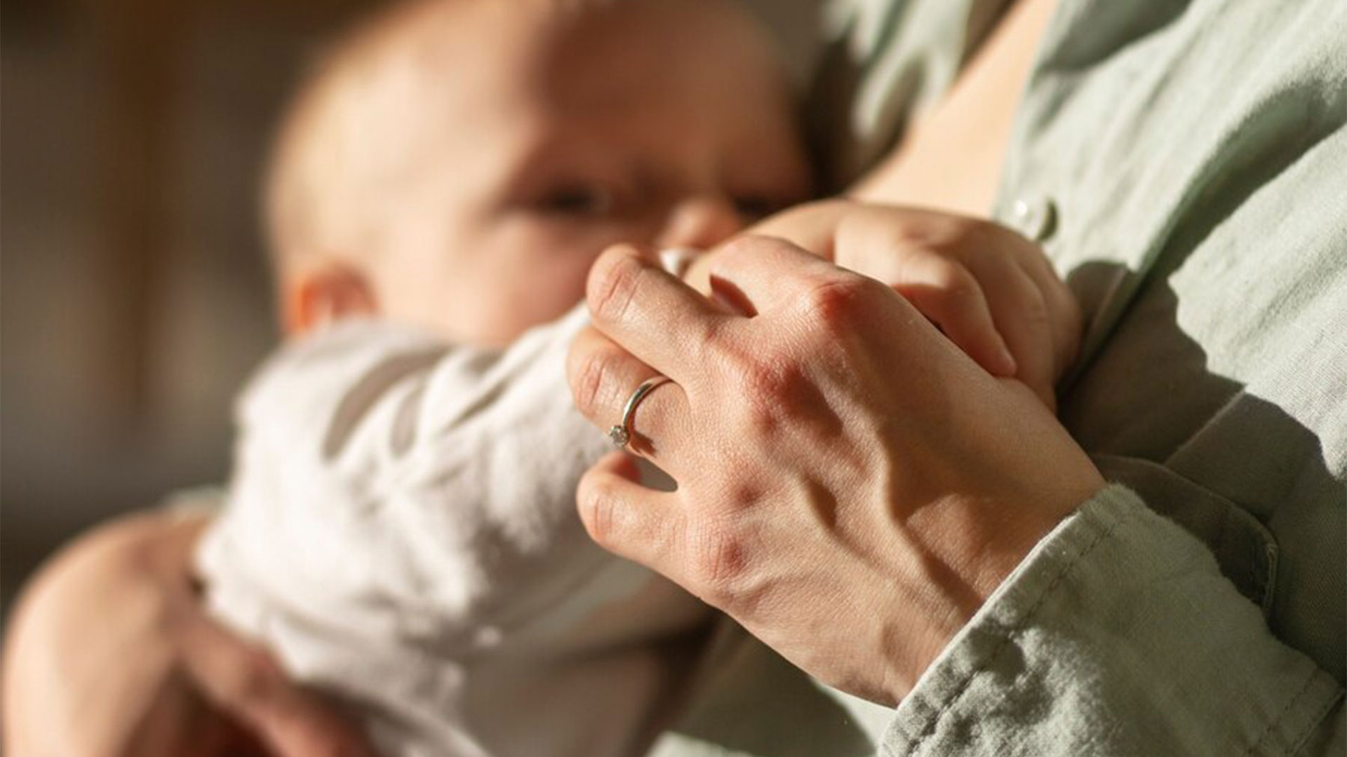 Mulher segurando mão do bebê enquanto amamenta