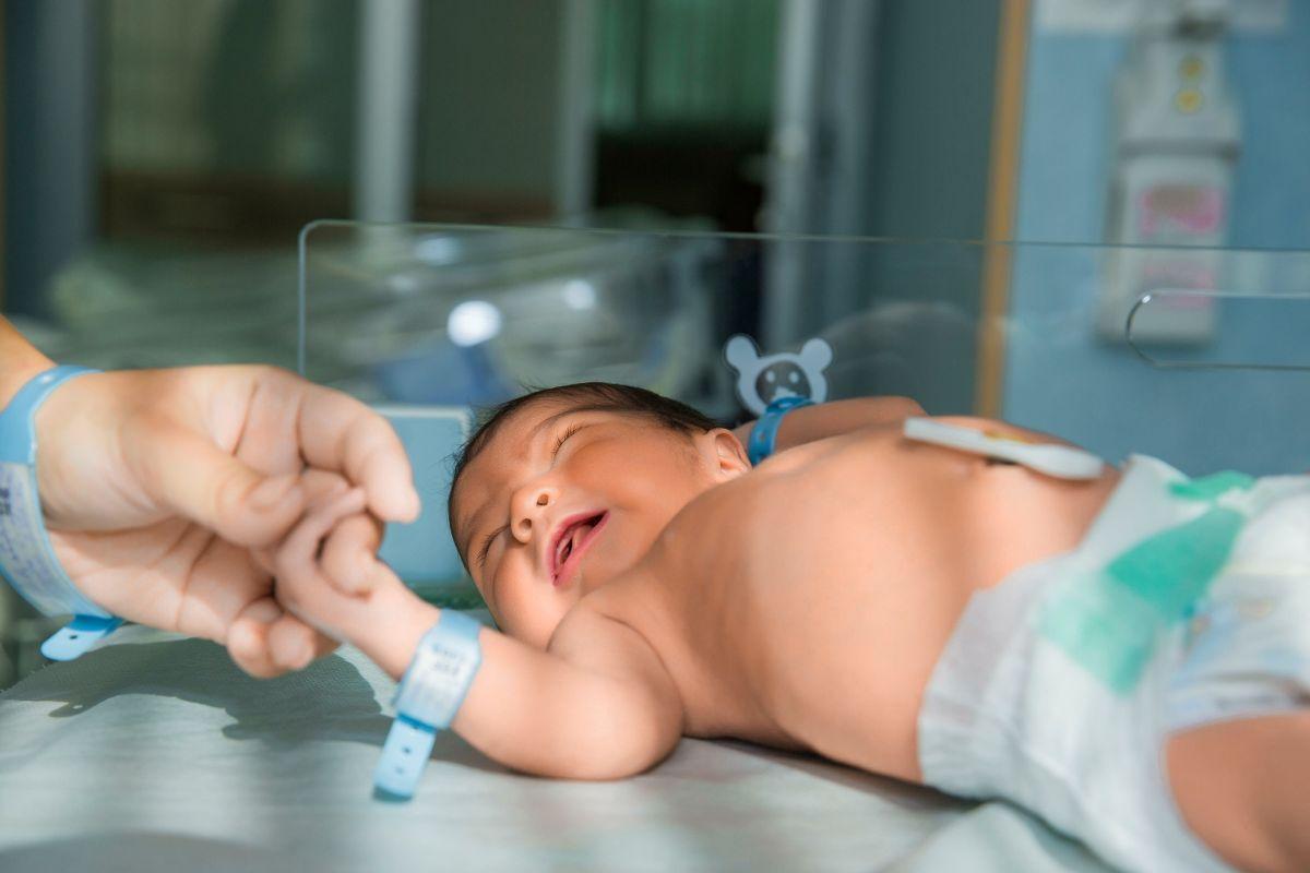 Mãe segura a mão da bebe na UTI
