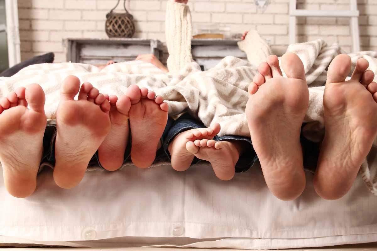 Pés de mãe, pai e filho, deitados na cama