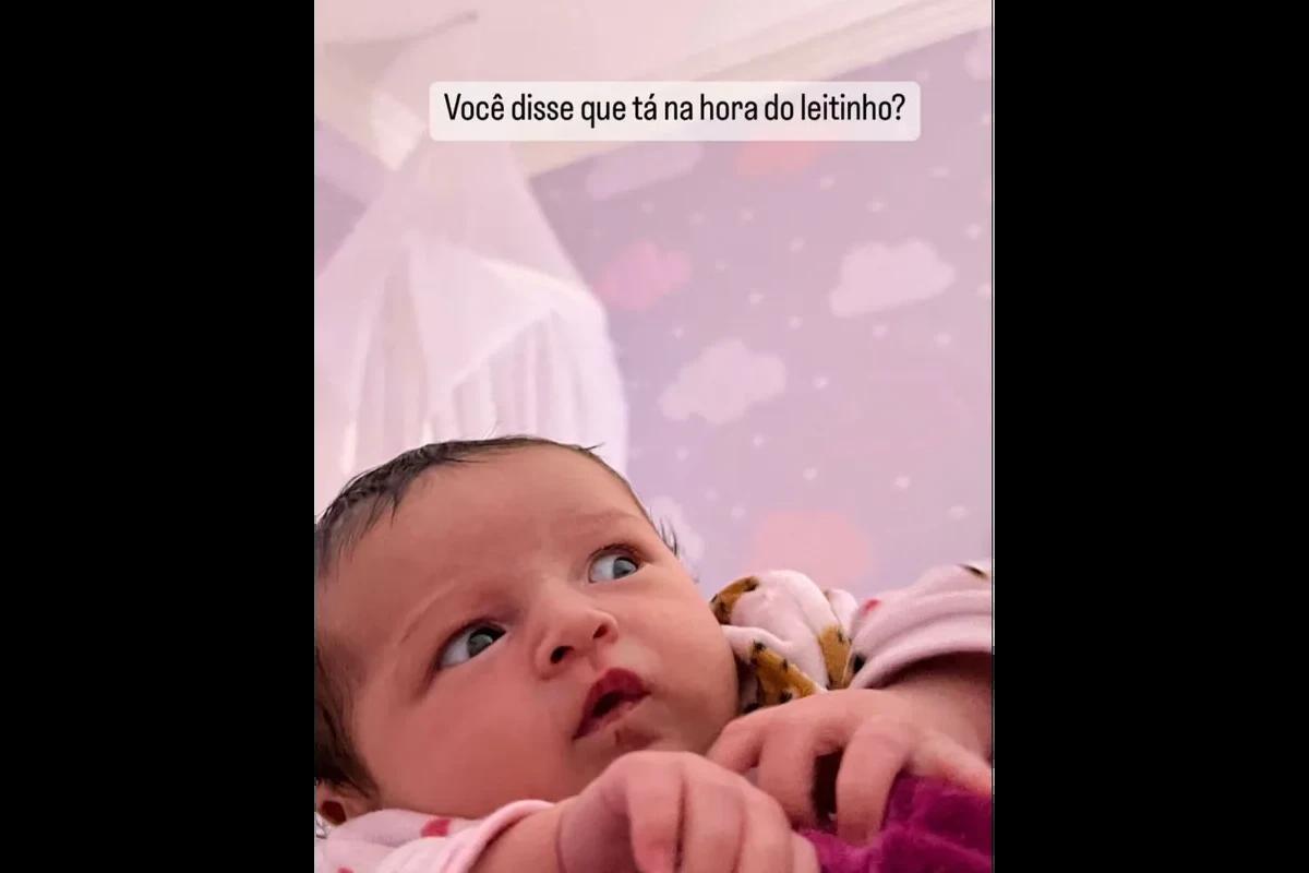 Bebe usando macação rosa em parede roxa