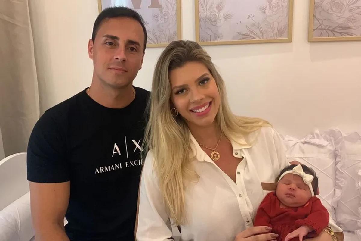 Homem com blusa preta, mulher lorira com blusa branca com bebe de colo