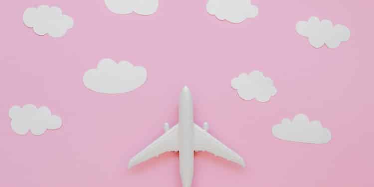 Avião de brinquedo e nuvens de papel em fundo rosa.