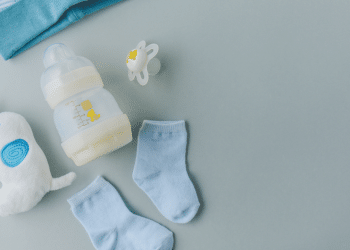 Mamadeira, chupeta, meias e brinquedo de bebê em fundo cinza