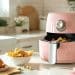 Airfryer rosada em uma cozinha branca com comidas em volta.