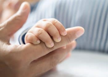 Bebê segura a mão da mãe, simbolizando a adoção.