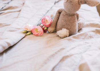 um ursinho na cama ao lado de flores cor de rosa