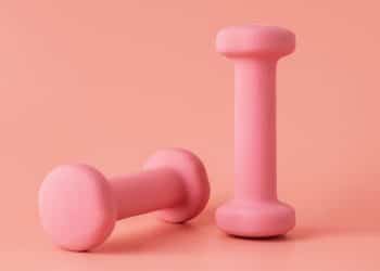 Dois pesos rosados de exercícios em um fundo da mesma cor.