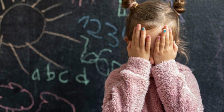 Menina com as mãos na frente do rosto com um fundo de lousa.