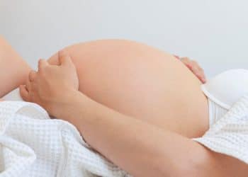 Close na barriga de uma mulher grávida vestindo branco, simbolizando o parto.