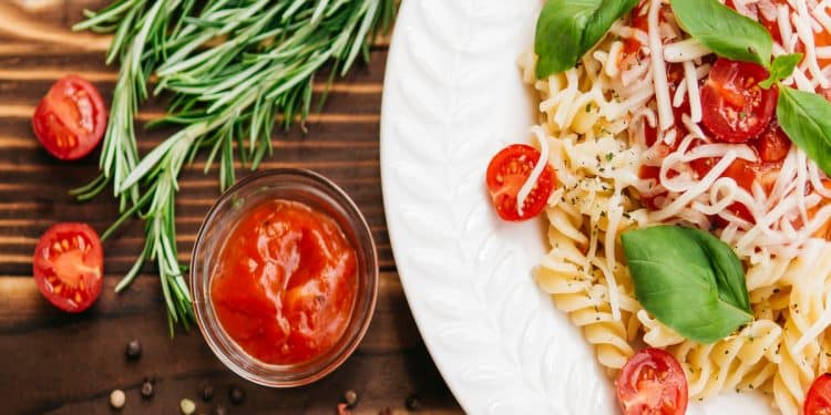 Prato de macarrão integral com tomate cereja em fundo de madeira.