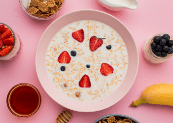 Prato com iogurte e outras frutas em volta, em um fundo cor de rosa.