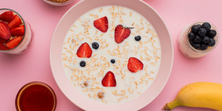 Prato com iogurte e outras frutas em volta, em um fundo cor de rosa.