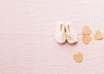 Sapato de recém-nascido com corações em volta em um fundo rosa.