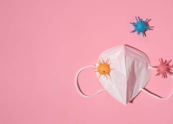 Máscara com vírus coloridos em fundo rosa, representando a dor de garganta.