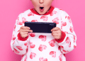 Criança com celular na mão e um pijama rosa e branco