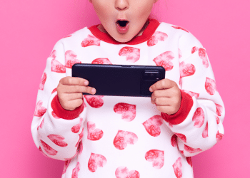 Criança com celular na mão e um pijama rosa e branco