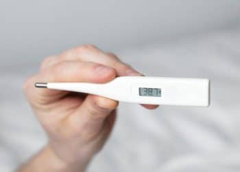 Pessoa segurando um termômetro que indica febre.