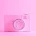 Câmera rosa bebê em frente a um fundo da mesma cor, representando um ensaio fotográfico infantil.