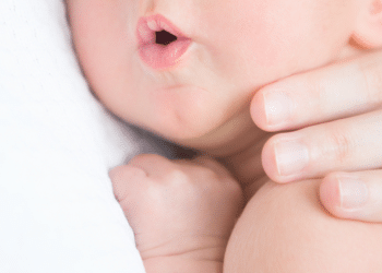 Criança deitada no colo da mãe com a boca aberta