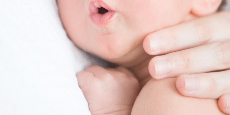 Criança deitada no colo da mãe com a boca aberta