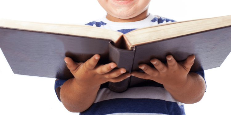 Criança com um livro grande na mãe e sorrindo. Na imagem, ela está em um fundo branco