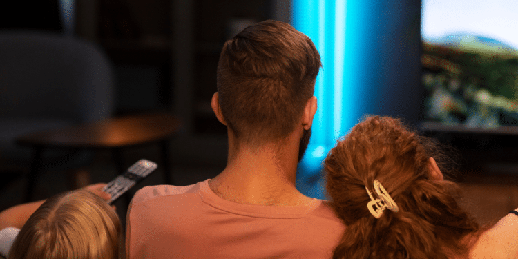 Um pai, uma mãe e um filho assistindo alguma coisa na televisão