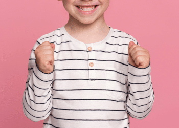 Sorrios de uma criança (menino), com uma camisa listrada e um fundo rosa