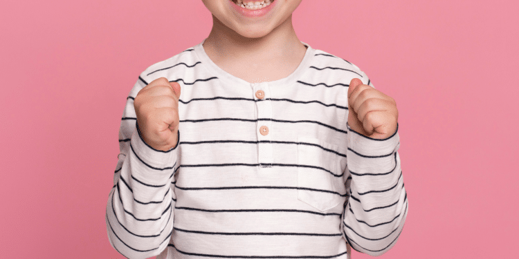 Sorrios de uma criança (menino), com uma camisa listrada e um fundo rosa