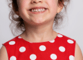 Criança sorrindo com um vestido de bolinhas brancas e vermelho