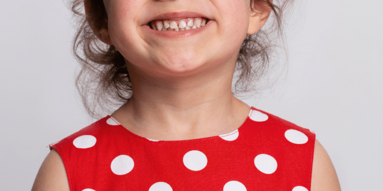 Criança sorrindo com um vestido de bolinhas brancas e vermelho