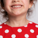 Criança sorrindo com um vestido de bolinhas brancas e vermelho
