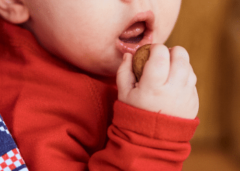 Bebê colocando um alimento na boca, o que parece ser um biscoito