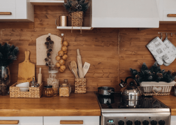 Uma cozinha completa com fogão, ármario, tábua de carne, alhos pendurados, panela encima do fogão