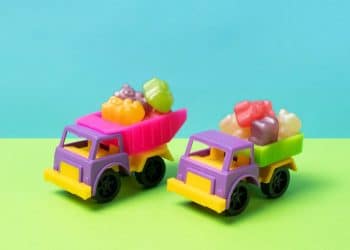 Brinquedos de caminhões coloridos com gomas em cima em um fundo azul e verde.