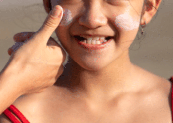 Menina sorrindo com uma mão passando protetor solar