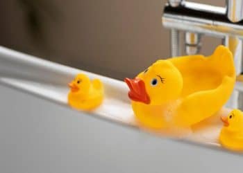 3 patos de borracha na beira de uma banheira representando o banho das crianças.