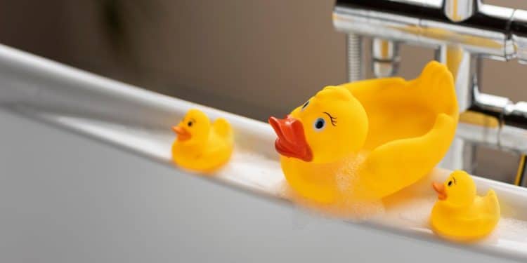 3 patos de borracha na beira de uma banheira representando o banho das crianças.