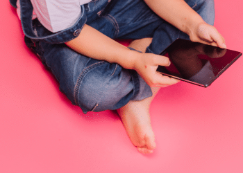 Criança segurando um tablet em um fundo rosa