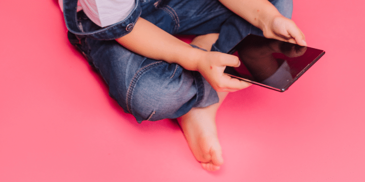 Criança segurando um tablet em um fundo rosa