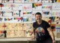 MENA agachado em frente a um mural com desenhos de crianças.