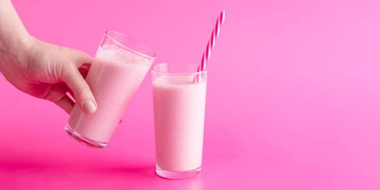 Dois copos de Nesquik natural ao lado de uma mão em um fundo rosa.
