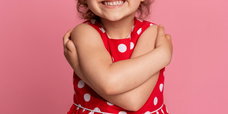 Criança sorrindo em um fundo rosa, com vestidos de bolinhas brancas