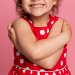 Criança sorrindo em um fundo rosa, com vestidos de bolinhas brancas