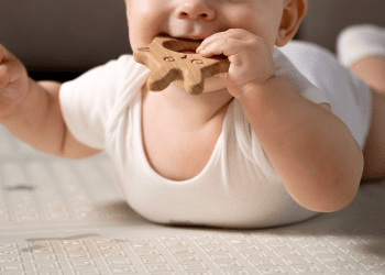 Bebê com um macaquinho branco e um brinquedo com a mão na boca