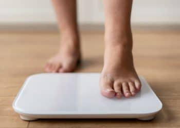 Criança subindo em uma balança, representando a obesidade infantil.