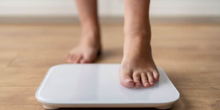 Criança subindo em uma balança, representando a obesidade infantil.