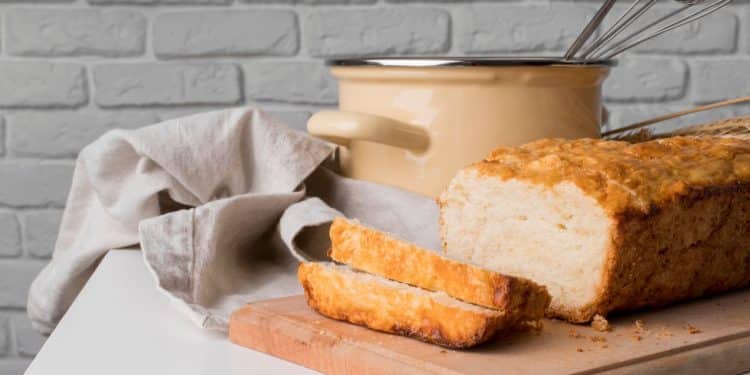 Pão de micro-ondas em cima de uma tábua de madeira com uma panela e uma parede de tijolos brancos atrás.