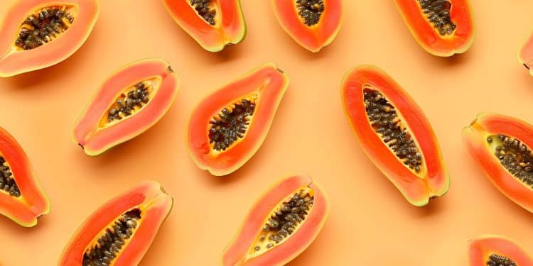 Várias unidades cortadas de mamão espalhadas em um fundo laranja claro.
