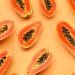 Várias unidades cortadas de mamão espalhadas em um fundo laranja claro.