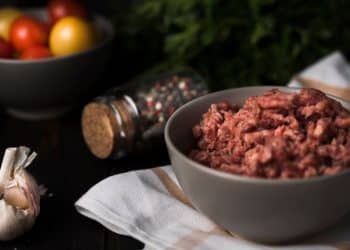 Carne moída em uma tigela com alho e vegetais atrás.